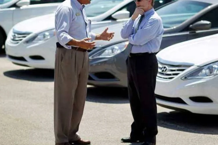 Homens conversando em um pátio com carros (Getty Images)