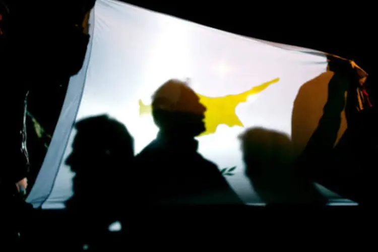 
	Pessoas seguram bandeira do Chipre durante protesto: pa&iacute;s recebeu &euro; 10 bilh&otilde;es em empr&eacute;stimos emergenciais do fundo de resgate da zona do euro em abril para evitar a fal&ecirc;ncia
 (Milos Bicanski/Getty Images)
