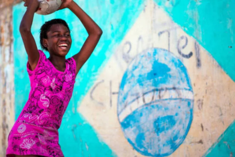 Garota brinca com bola de futebol em frente a bandeira do Brasil pintada em muro de favela do Rio de Janeiro (Buda Mendes/Getty Images)
