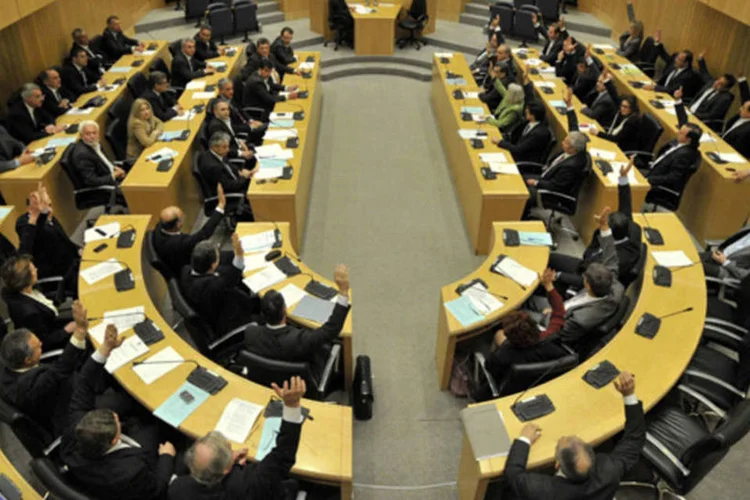 Parlamentares levantam as mãos para votar contra um controverso projeto de lei que taxaria depósitos em Nicósia, Chipre (Yiannis Nissiotis/Reuters)