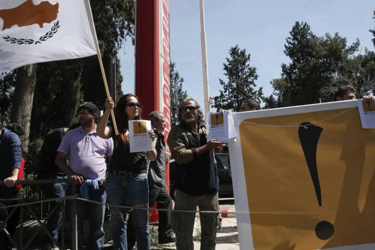 Manifestantes anti-resgate seguram faixa e uma bandeira cipriota durante passeata de estudantes pelo dia de Independência da Grécia, em Nicósia (Yorgos Karahalis)