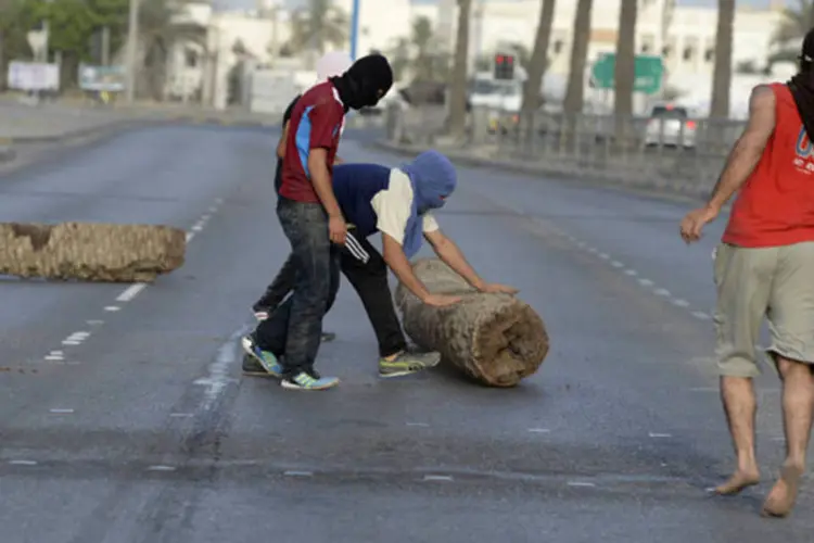 Manisfestante move tronco de árvore para bloquear uma estrada na vila de Sitra, sul da capital do Bahrein, Manama (Reuters)