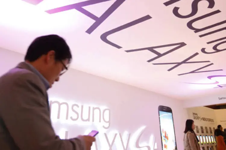 Visitante usando um smartphone passa em frente ao logo do Galaxy S4, durante seu lançamento na sede da Samsung, em Seul (Kim Hong-Ji/Reuters)