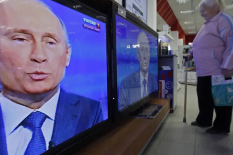 Mulher assiste televisores transmitindo o discurso em rede nacional do presidente russo Vladimir Putin em uma loja de eletrônicos em Sochi (Alexander Demianchuk/Reuters)