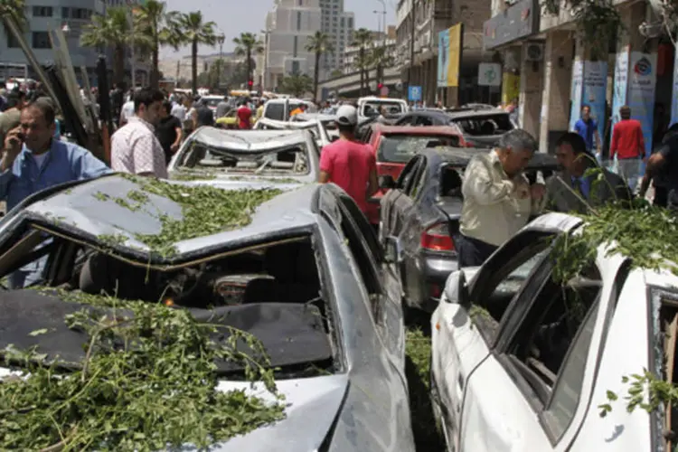 Pessoas caminham em uma rua com edifícios e carros danificados após explosão na praça Marjeh, em Damasco (Khaled al-Hariri/Reuters)