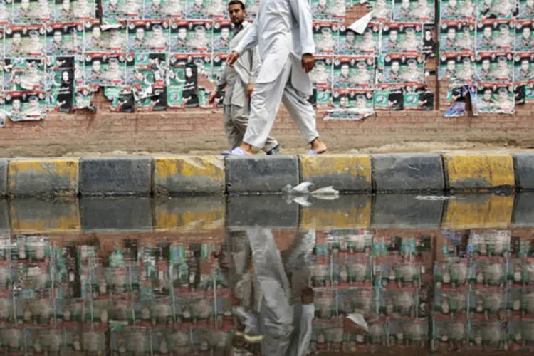 Pessoas caminham em frente a uma parede coberta de cartazes eleitorais no centro velho de Lahore, Paquistão (Damir Sagolj/Reuters)