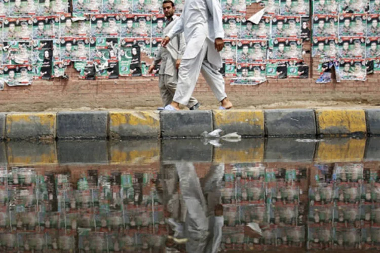 Pessoas caminham em frente a uma parede coberta de cartazes eleitorais no centro velho de Lahore, Paquistão (Damir Sagolj/Reuters)