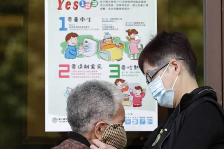 Mulher ajuda outra mulher a vestir máscara diante de um pôster explicativo para a prevenção contra o vírus H7N9 da gripe aviária, em Taipei, Taiwan (Pichi Chuang/Reuters)