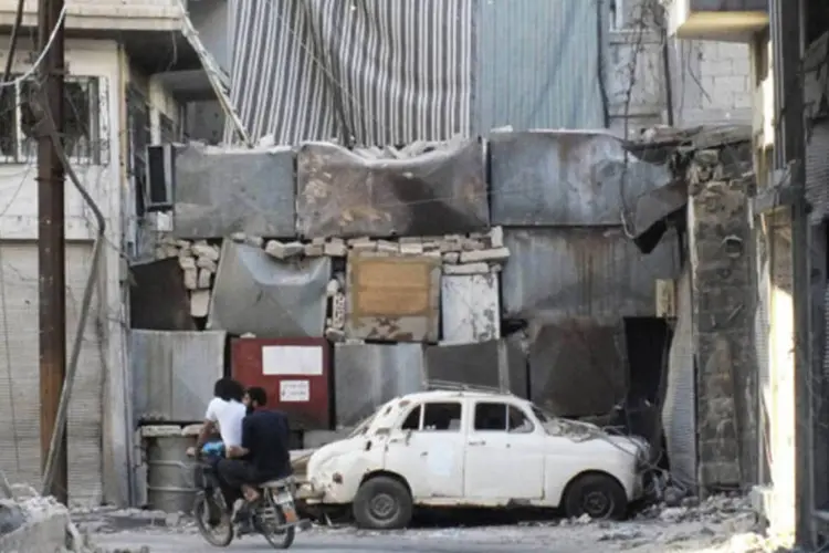 Pessoas andando de motocicleta entre carros e prédios danificados por, segundo ativista, bombas das forças leais do presidente sírio Bashar al-Assad, em Homs (Yazan Homsy/Reuters)