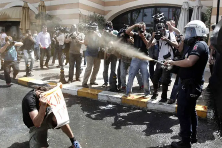 Polícia de choque turca lança gás lacrimogêneo contra manifestante segurando cartaz durante protesto contra a destruição de árvores em um parque, na praça Taksim, em Istambul (Osman Orsal/Reuters)