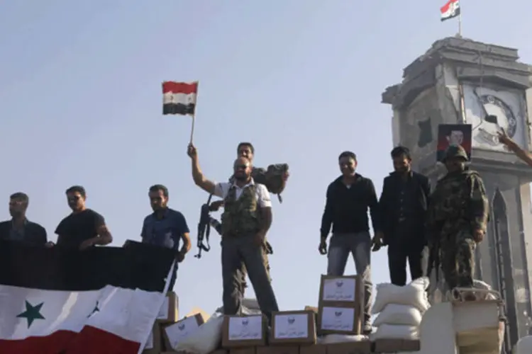 Soldados e civis leais ao regime de Bashar al-Assad seguram bandeiras da Síria em Qusair, após o exército retomar o poder na cidade (Mohamed Azakir/Reuters)