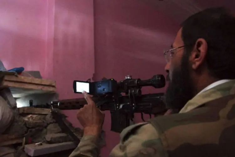 Membro do exército livre da Síria aponta a sua arma através de um buraco enquanto usa uma câmera para fotografar a cena em Deir al-Zor (Khalil Ashawi/Reuters)