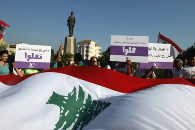 Ativistas e membros de organizações da sociedade civil seguram cartazes enquanto carregam uma bandeira gigante do Líbano durante um protesto contra o Parlamento, em Beirute (Sharif Karim/Reuters)