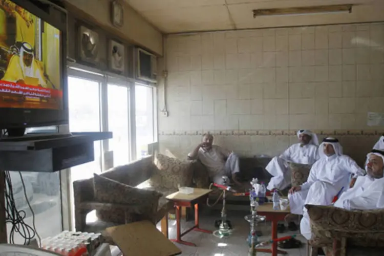 Homens assistem o discurso de renúncia do então emir do Catar xeique Hamad bin Khalifa al-Thani em uma televisão em um bar de Doha (Mohammed Dabbous/Reuters)