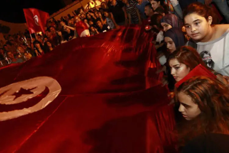 Pessoas seguram uma bandeira gigante da Tunísia durante uma cerimônia em tributo aos soldados mortos durante uma emboscada na praça Kasbah, em Túnis  (Anis Mili/Reuters)