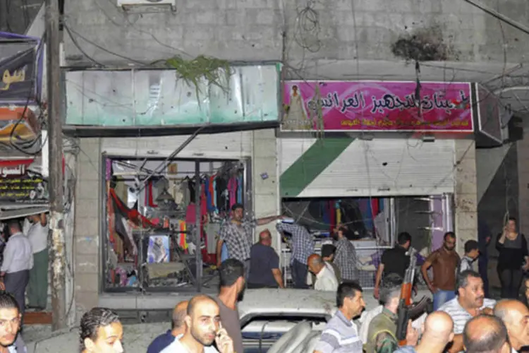 Pessoas em torno dos destroços de um carro a bomba que explodiu no distrito de Jaramana, sudeste de Damasco (SANA/Divulgação via Reuters)