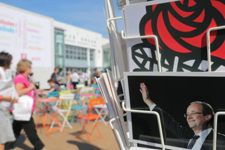 Pessoas passam por estante com cartões postais do presidente François Hollande no encontro do Partido Socialista Francês, em La Rochelle (Stephane Mahe/Reuters)