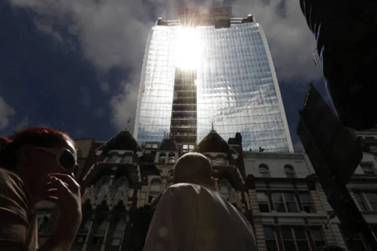 
	Pedestres caminham atrav&eacute;s dos fortes raios refletidos pelo: o feixe de luz causado pelas curvas do arranha-c&eacute;u chegou em setembro a mais de 110&ordm;C e derreteu partes de carros
 (Suzanne Plunkett/Reuters)
