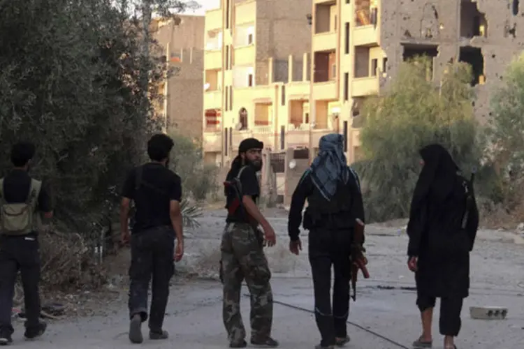 Guerrilheiros do Exército Livre da Síria caminham em rua danificada em Deir al-Zor, Síria (Mohamad Alderi/Reuters)