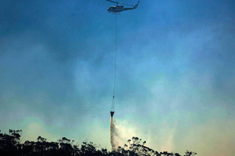 
	Helic&oacute;ptero joga &aacute;gua em foco de inc&ecirc;ndio na Austr&aacute;lia: as equipes continuam os trabalhos de combate a 66 inc&ecirc;ndios, 24 dos quais est&atilde;o fora de controle
 (REUTERS/David Gray)