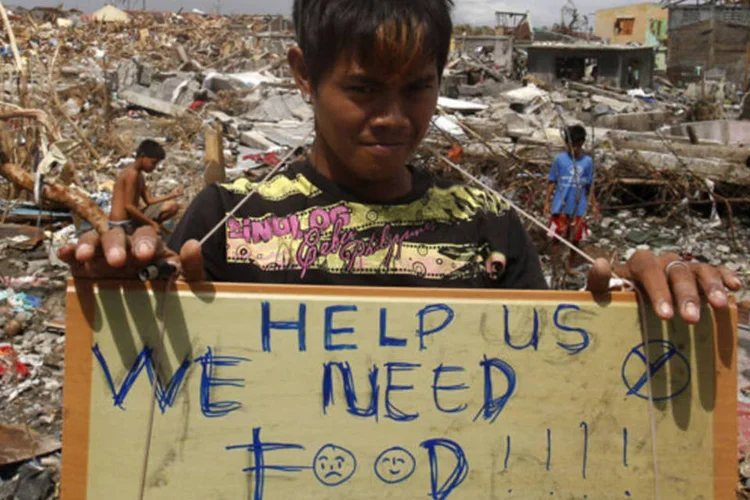Vítima do supertufão Haiyan segura uma placa em que pede por comida, em meio às ruinas das casas destruídas em Tanauan, na província de Leyte, região central das Filipinas (Erik De Castro/Reuters)