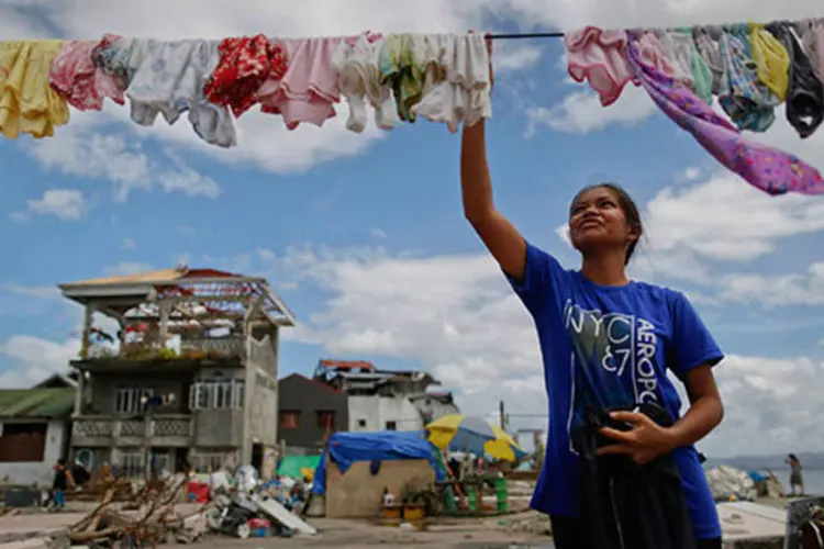 Mulher estende roupa no varal em frente à sua casa destruída pela passagem do tufão Haiyan, nas Filipinas (Ho/AFP)