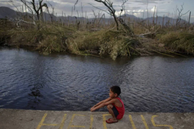 Garoto sentado sobre uma mensagem de pedido de ajuda em uma área atingida pelo tufão Haiyan, em Palo, nas Filipinas (John Javellana/Reuters)