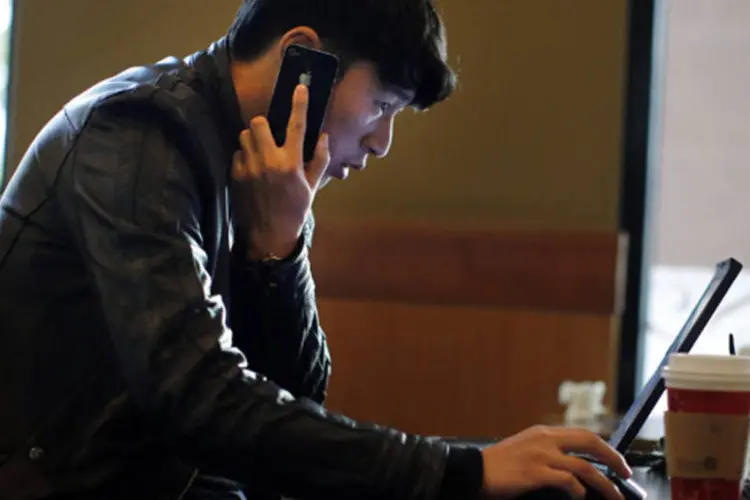 Homem fala no telefone enquanto navega na internet em seu notebook em um bar no centro de Xangai, na China (Carlos Barria/Reuters)