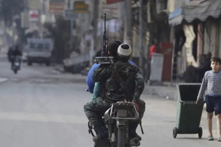 Um garoto puxa uma lata de lixo conforme passam soldados do Exército Sírio Livre, carregando suas armas, em uma moto em uma rua em Deir al-Zor, no leste da Síria (Khalil Ashawi/Reuters)