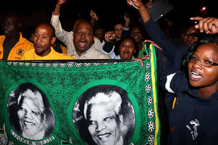 
	Pessoas entoam slogans em frente &agrave; casa de Nelson Mandela: agitando bandeiras, com flores e can&ccedil;&otilde;es, centenas de pessoas de diferentes ra&ccedil;as e religi&otilde;es homenageiam o grande her&oacute;i&nbsp;
 (REUTERS/Siphiwe Sibeko)