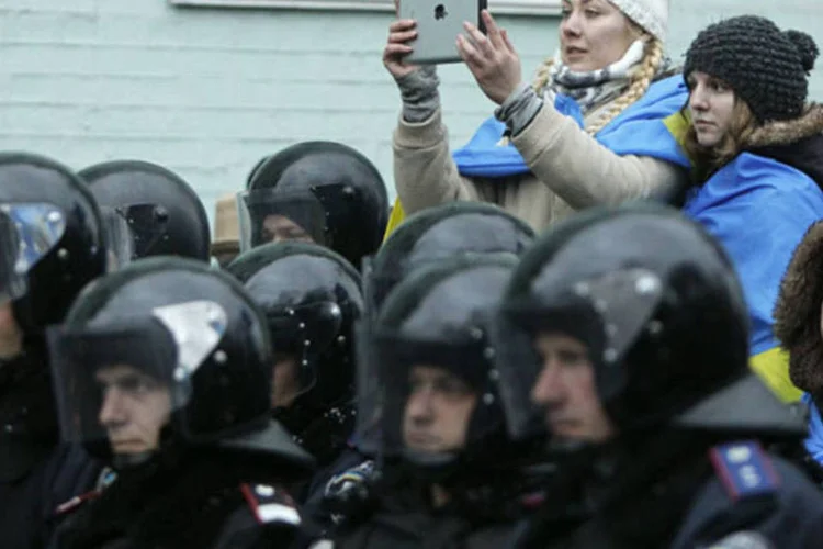 Apoiador do Partido das Regiões tira fotos de manifestação em favor da integração da UE, com a tropa de choque e funcionários do Ministério do Interior bloqueando rua, no centro de Kiev (Gleb Garanich/Reuters)