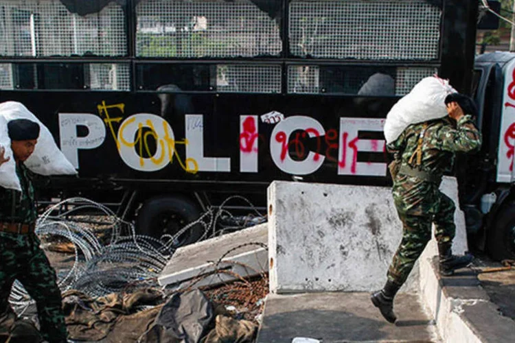 Soldados tailandeses carregam sacos de gelo enquanto passam por um caminhão de polícia destruído próximo à Casa do Governo, onde aconteceram protestos antigovernamentais, em Bangcoc (REUTERS/Athit Perawongmetha)