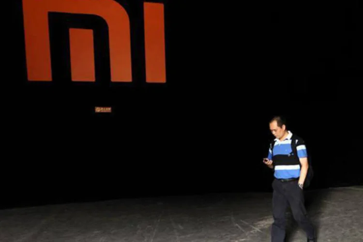 Homem checa o celular enquanto passa por logo da Xiaomi, durante cerimônia de lançamento do Phone 2 da empresa, em Pequim (Jason Lee/Reuters)