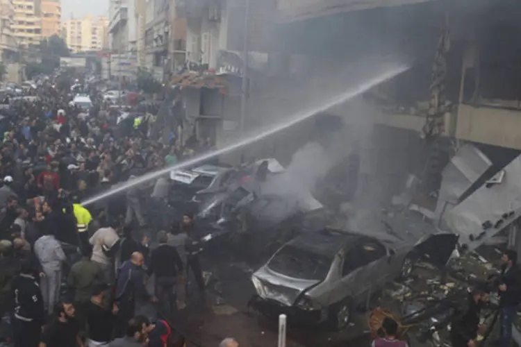 Pessoas se aglomeram ao redor de bombeiros que tentam apagar as chamas provocadas por uma explosão no sul de Beirute (Issam Kobeisi/Reuters)