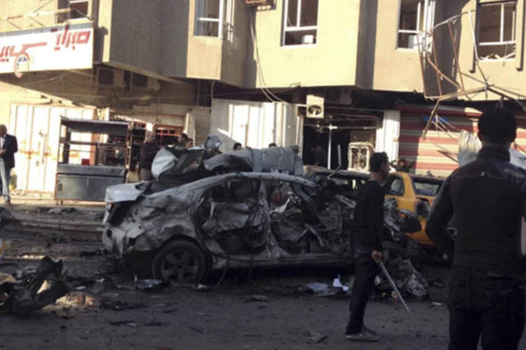 Pessoas observam o local de um ataque com um carro-bomba em Bagdá, no Iraque (Thaier Al-Sudani/Reuters)