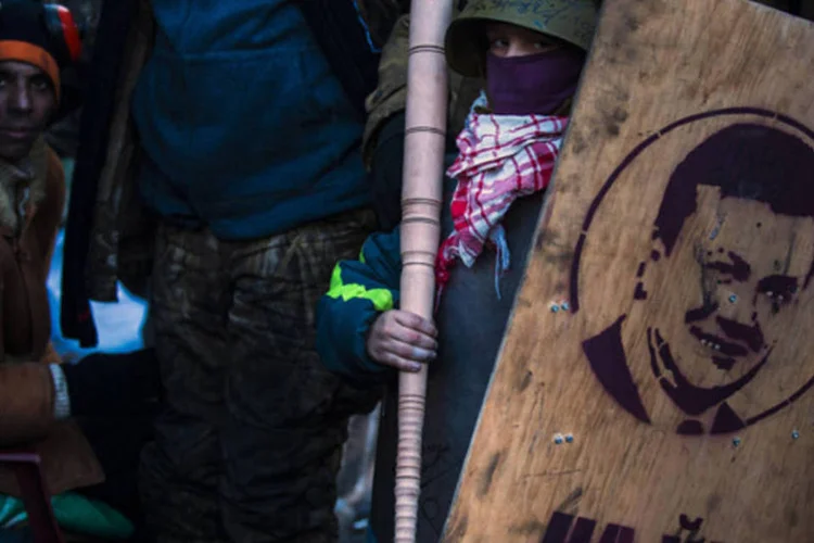 Homem segura um bastão e um escudo com um grafite do presidente ucraniano, Viktor Yanukovich, em uma barricada contrário ao governo, em Kiev (Thomas Peter/Reuters)