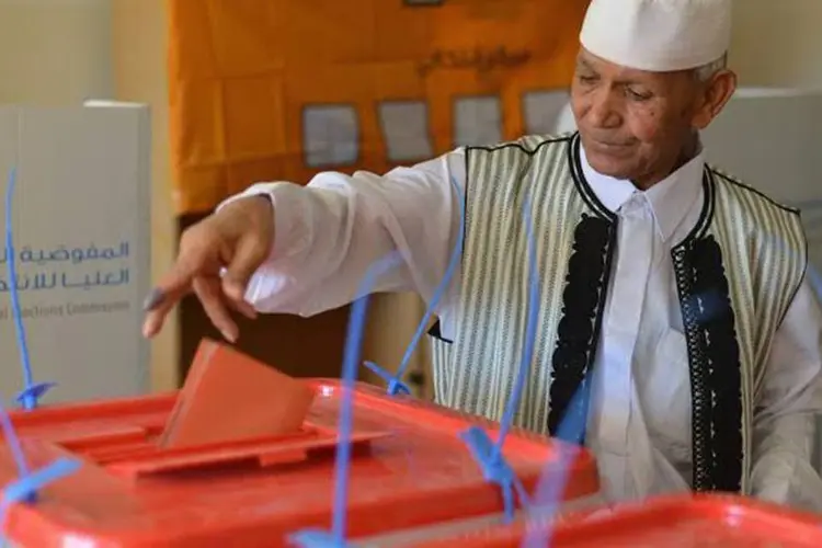 Eleitor com vestes tradicionais insere seu voto na urna durante eleições na Líbia (REUTERS/Saddam Alrashdy)