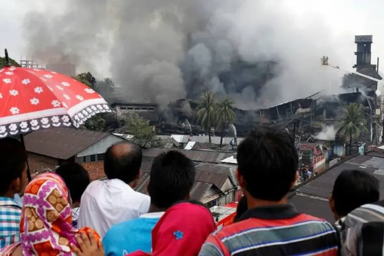 
	Pessoas observam fuma&ccedil;a ap&oacute;s inc&ecirc;ndio em f&aacute;brica de embalagens Bangladesh: caldeira explodiu
 (Mohammad Ponir Hossain/Reuters)