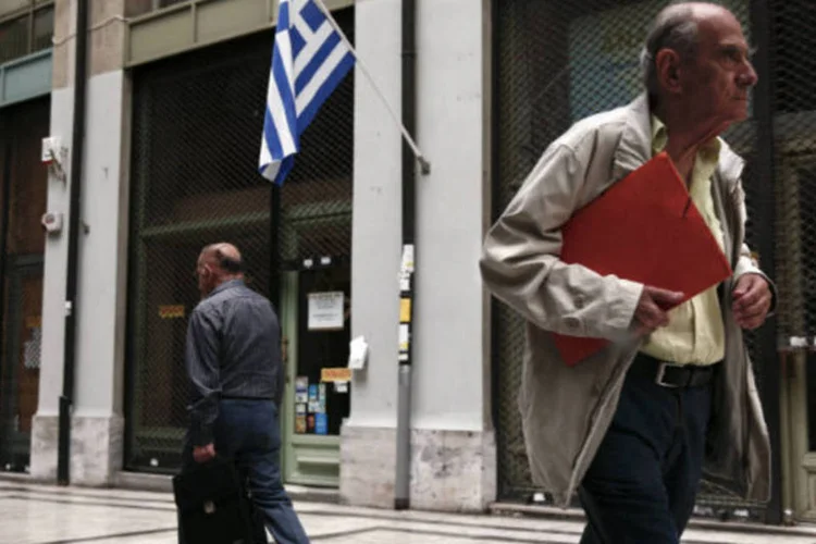 
	Pessoas passam por bandeira da Gr&eacute;cia em rua do centro de Atenas
 (REUTERS/Yorgos Karahalis)