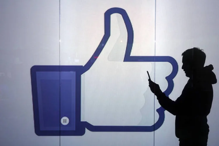 Pessoa usando smartphone em frente ao logo do Facebook (Chris Ratcliffe/Bloomberg)