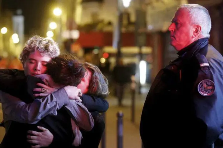 Três pessoas se abraçam perto da casa de shows Bataclan em Paris (Christian Hartmann/Reuters)