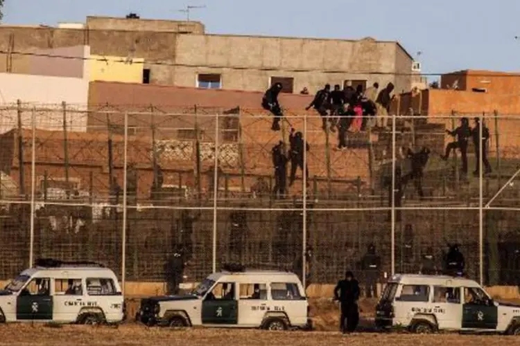 
	Agentes da Guarda Civil escalam cerca para retirar imigrantes que est&atilde;o no alto, em Melilla, Espanha
 (José Colón/AFP)
