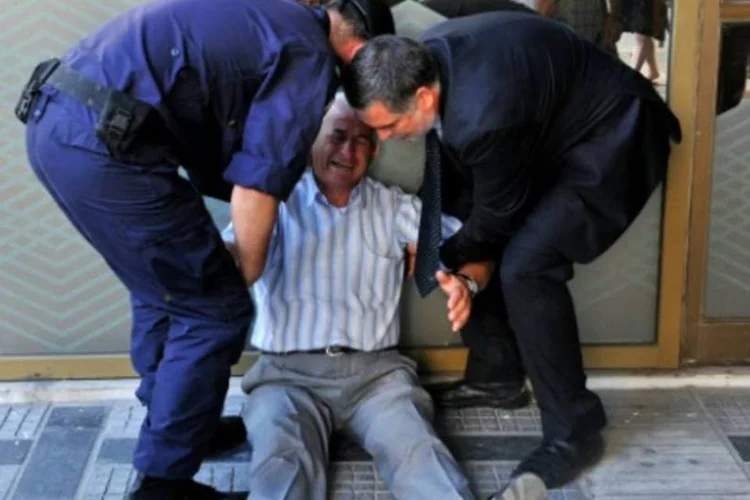 Aposentado grego é ajudado por funcionário de agência bancária e por policial, após passar mal por não conseguir sacar dinheiro, em Tessalônica (Sakis Mitrolidis/AFP)