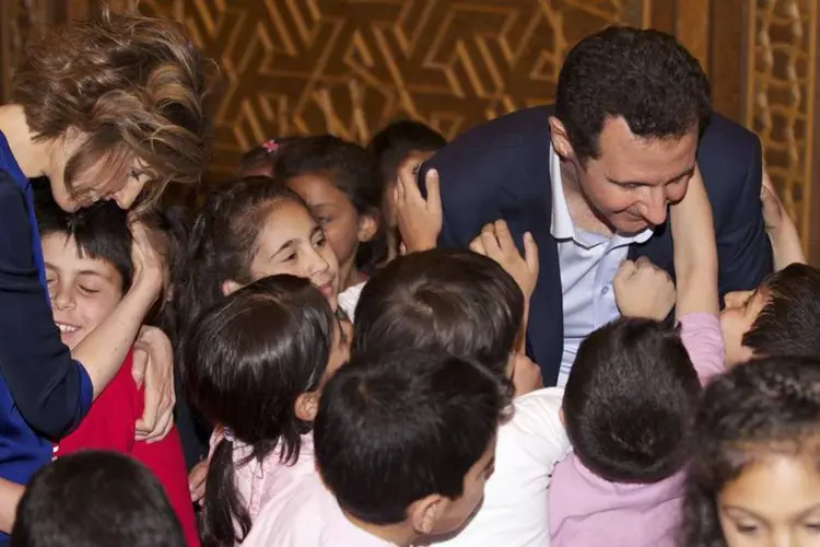 Bashar al-Assad, presidente sírio, e sua esposa, Asma, cercado de crianças: o casal, sorridente, abraça e dá mostras de afeto aos menores (Sana/Handout via Reuters)