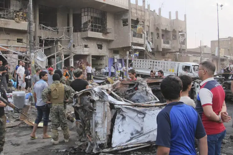 Pessoas e combatentes xiitas em local de explosão de carro-bomba em Bagdá (Reuters)