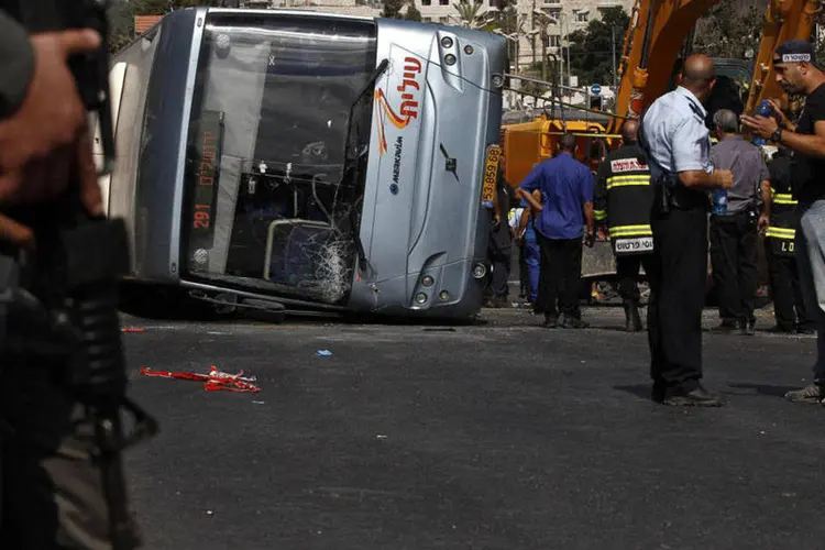 Policiais israelenses ao lado de um ônibus virado por uma escavadeira, em Jerusalém (Siegfried Modola/Reuters)