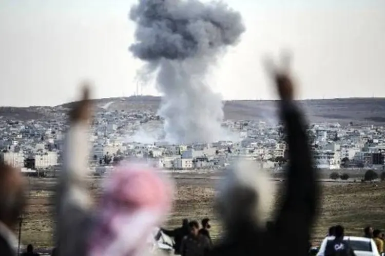 
	Pessoas observam fuma&ccedil;a na cidade de Kobane: na madrugada deste domingo houve novos ataques a&eacute;reos contra o EI na cidade
 (Bulent Kilic/AFP)