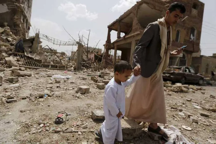 Homem e criança passam por local atingido por ataque da coalizão saudita em Sanaa, capital do Iêmen (REUTERS/Khaled Abdullah)