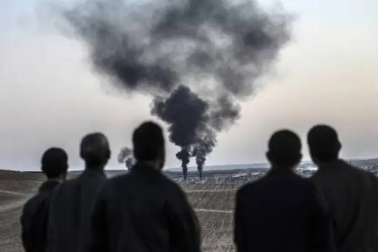 Homens observam fumaça saindo de Kobane: jihadistas já haviam apedrejado até a morte várias mulheres acusadas de adultério (Bulent Kilic/AFP)