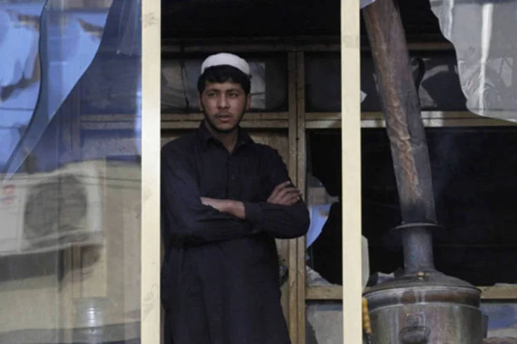 Afegão olha por uma janela quebrada o local da explosão de um ataque suicida na cidade de Jalalabad, no Afeganistão (Parwiz/Reuters)